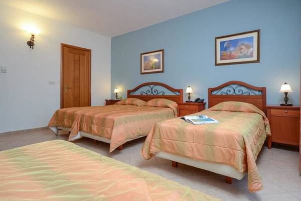 Doppelzimmer mit zwei Betten im Naxos Resort Beach Hotel, beide mit orangen Decken, neben Nachttischen mit Lampen.