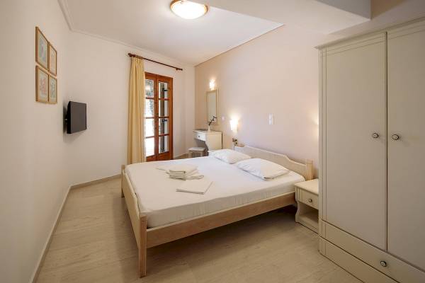Ein Schlafzimmer im Proteas Hotel mit einem Bett, einem Nachttisch, einem Schrank und einer Wand mit einem Fernseher und Kunstwerken.