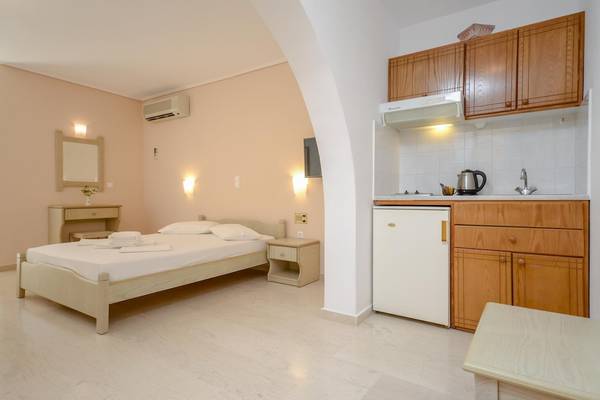 Innenansicht des Schlafzimmers im Proteas Hotel & Suites mit Bett, Nachttisch und Küche.