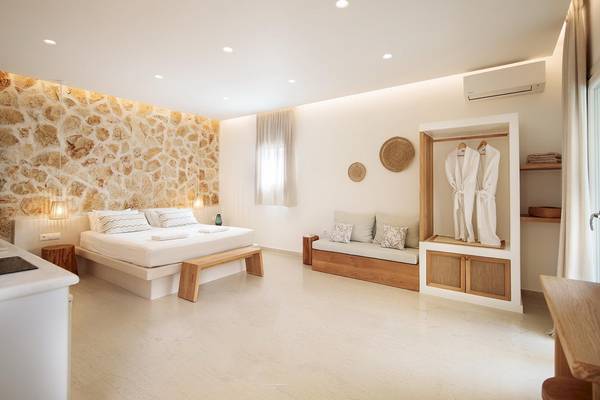 Innenansicht des Schlafzimmers im Proteas Hotel & Suites mit Steinwand, Doppelbett, Holzbank und Sitzbank.