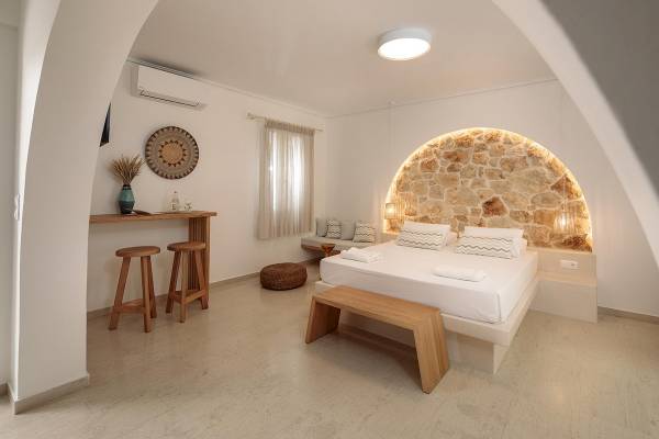 Innenansicht eines Schlafzimmers im Proteas Hotel & Suites mit weißer Bettwäsche, Holzmöbeln und Steinwand.