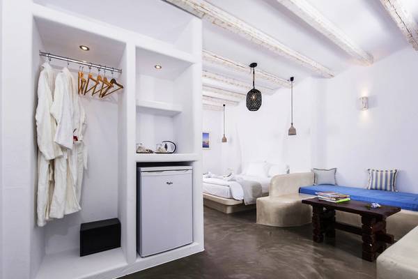 Innenansicht eines Zimmers im Cycladic Islands Hotel & Spa mit einem Bett, einer Couch, einem Tisch, einer Lampe und einem Kühlschrank.