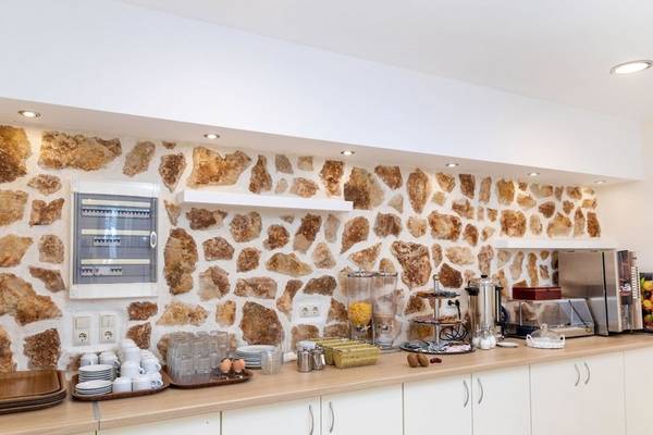 Frühstücksbereich im Hotel Golden Coast mit Steinwand, Frühstücksbuffet und Kaffeemaschine.