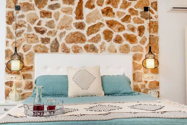Schlafzimmer mit Steinwand und blauer Bettwäsche, Kissen und Glasflasche auf dem Bett.