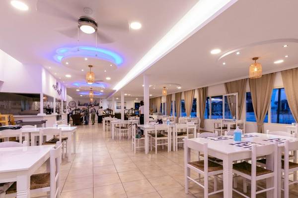 Innenansicht des Mikri Vigla Hotel Restaurants mit weißen Tischen und Stühlen und dekorativen Deckenlampen.