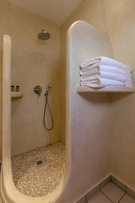 Eine Dusche im Mikri Vigla Hotel mit weißen Fliesen und Handtüchern auf einem Regal.