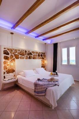 Schlafzimmer im Mikri Vigla Hotel mit Steinwand, weißer Bettwäsche und Seeblick
