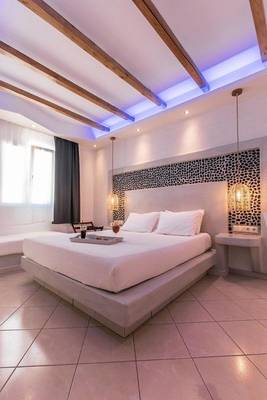 Schlafzimmer im Mikri Vigla Hotel mit Bett, Kissen, Tisch und dekorativen Beleuchtungselementen.
