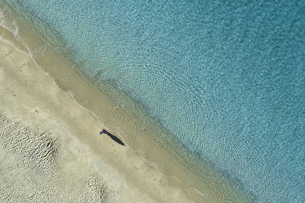Luftaufnahme eines Strandes mit einer Person, die am Rand des Wassers steht