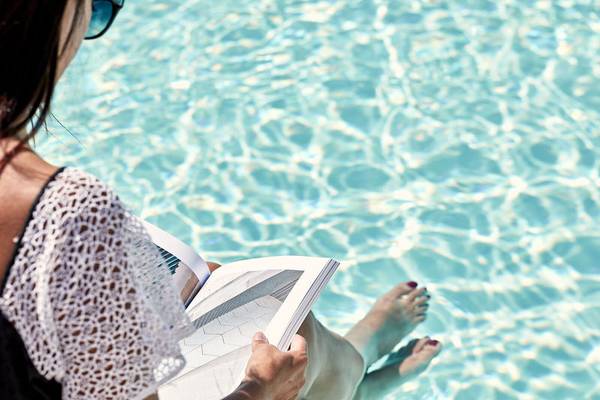 Frau sitzt im Schwimmbad und liest ein Buch