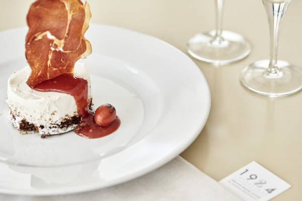 Ein Gericht auf einem weißen Teller serviert, dekoriert mit einem Stück Prosciutto, einer roten Soße und einer kleinen Tomate.