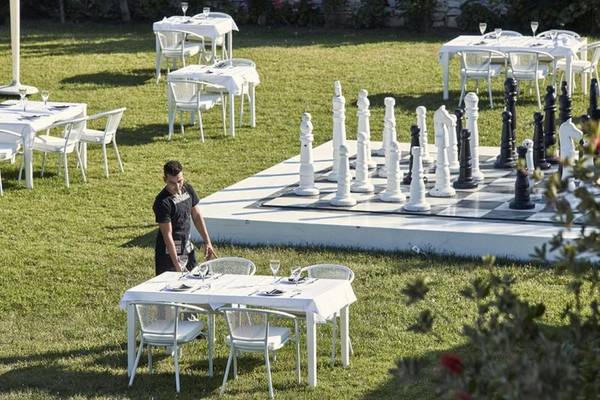 Ein Angestellter des Lagos Mare Hotels bereitet einen Tisch im Freien für Gäste vor, mit einem großen Schachspiel im Hintergrund.