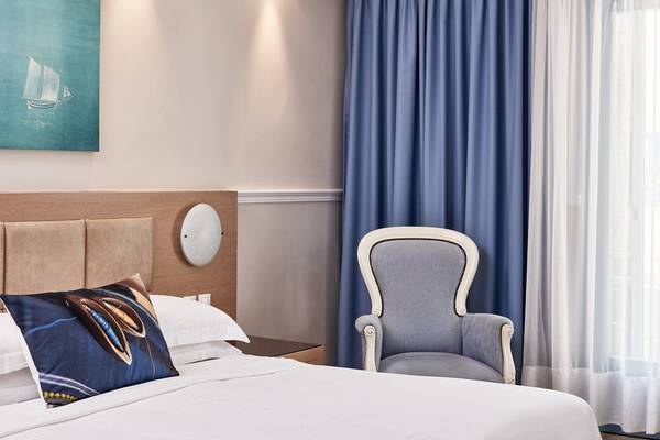 Foto von einem Hotelzimmer im Lagos Mare Hotel mit einem Bett, einem Stuhl und Vorhängen.