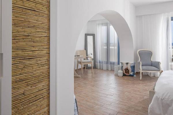 Innenansicht eines Zimmers im Lagos Mare Hotel mit einem hölzernen Boden, einer Wand aus Bambus, einem Bett, einem Stuhl, einem Tisch und einem Spiegel.