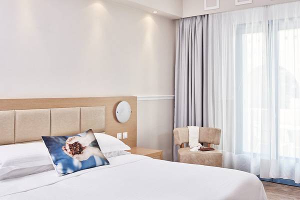 Schlafzimmer im Hotel Lagos Mare mit einem Bett, Kissen und einem Fenster mit Vorhängen.