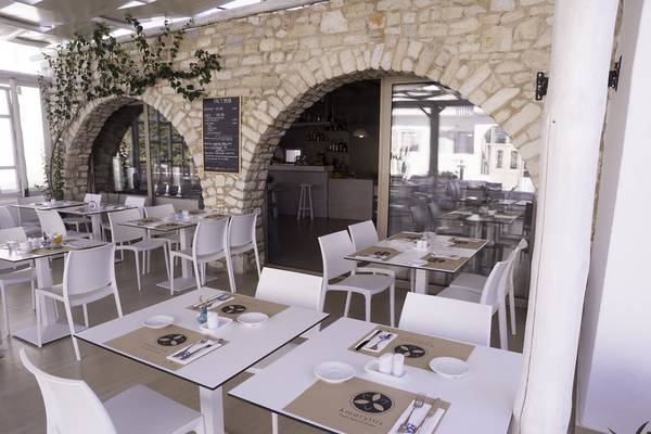 Innenbereich des Amaryllis Paros Beach Hotels mit weißen Tischen und Stühlen, Steinmauer und offenen Türen.