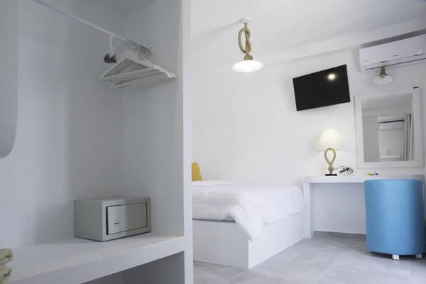 Innenansicht eines Zimmers im Amaryllis Paros Beach Hotel mit weißem Bett, Schreibtisch und blauem Stuhl.