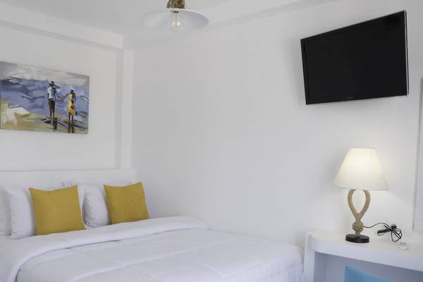 Schlafzimmer im Amaryllis Paros Beach Hotel mit weißem Bett, gelben Kissen und maritimem Bild.