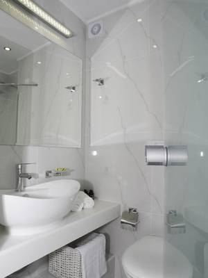 Modernes Badezimmer im Amaryllis Paros Beach Hotel mit weißen Fliesen, einem Waschbecken und einem Spiegel.