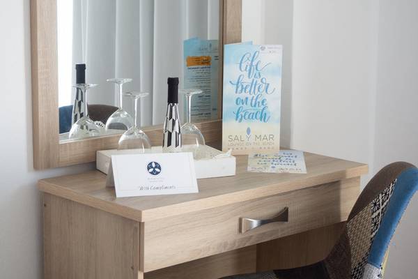 Zimmer im Amaryllis Paros Beach Hotel mit Schreibtisch, Stuhl, Spiegel und Willkommensgeschenk.