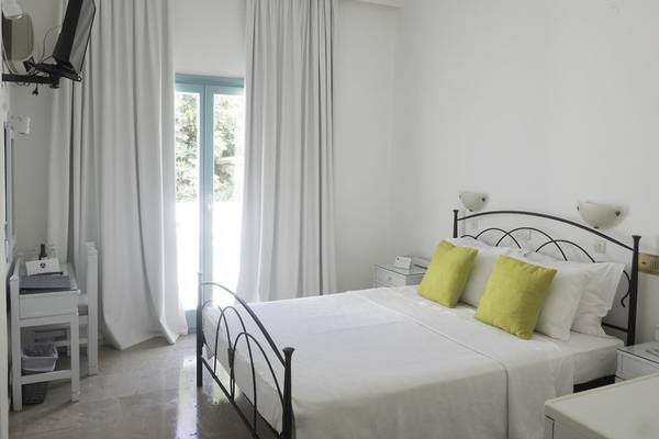 Schlafzimmer im Amaryllis Paros Beach Hotel mit einem Bett, weißen Laken, grünen Kissen und einer Aussicht auf den Garten.