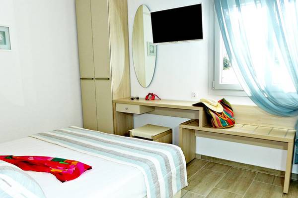 Doppelbettzimmer im Amaryllis Paros Beach Hotel mit weißem Bett, Kleiderschrank, Spiegel und Fernseher.