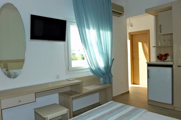 Innenansicht eines Hotelzimmers mit Schreibtisch, Stuhl, Bett, Fernseher und Kühlschrank.