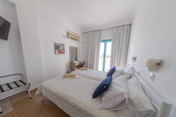 Doppelzimmer im Amaryllis Paros Strand Hotel mit zwei Betten, weißem Dekor und Aussicht durch eine Glastür.