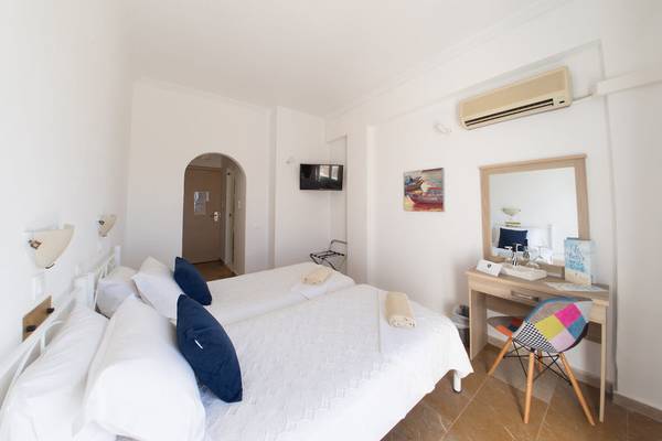 Schlafzimmer im Amaryllis Paros Beach Hotel mit zwei Betten, weißem Bettwäsche, blauen Kissen und einem Fernseher.