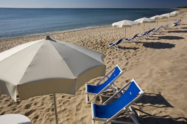 Strand mit weißen Sonnenschirmen und blauen Liegen am Meer