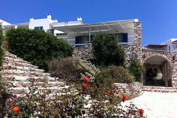 Außenansicht des Paros Agnanti Resorts & Spa mit Steinmauern und roten Rosen.