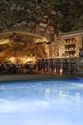 Ein Hotelpool und Bar mit Steinwänden und beleuchteten Tischen und Stühlen.