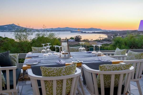 Außenbereich des Paros Agnanti Resorts & Spa mit Tisch und Stühlen, Blick auf den Sonnenuntergang und das Meer.