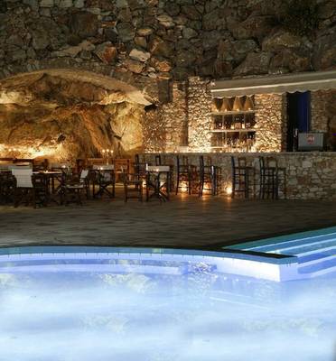 Pool im Paros Agnanti Resort & Spa mit steinerner Umgebung und beleuchteten Tischen.