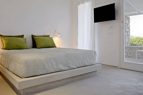 Schlafzimmer im Paros Agnanti Resort & Spa mit einem Bett, grünen Kissen, Fernseher und einer offenen Tür.