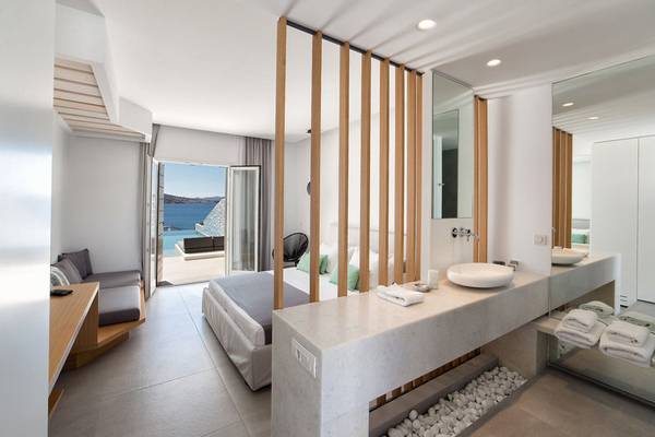 Innenansicht eines Hotelzimmers im Paros Agnanti Resort & Spa mit Bett, Badezimmer und Meerblick.