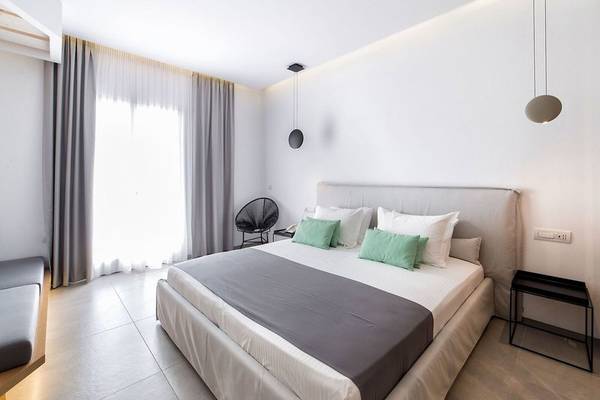 Schlafzimmer im Paros Agnanti Resort & Spa mit einem Doppelbett, grauen und grünen Kissen, weißem Kopfteil und modernen Lampen.