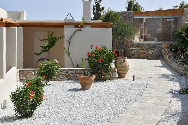 Außenbereich des Mythic Hotels mit Steinmauer, Steinweg und Blumen.