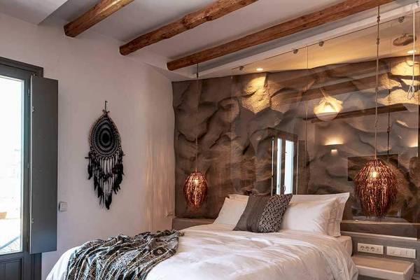 Schlafzimmer im Mythic Hotel mit Steinwand, Holzbalken, Bett, Decken und Lampen.