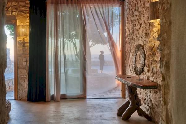 Innenansicht eines Zimmers im Mythic Hotel mit Blick durch einen Vorhang auf eine Person.