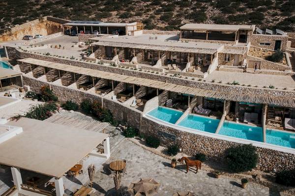 Luftaufnahme des Mythic Hotels mit Swimmingpools und einem braunen Pferd vor dem Gebäude.