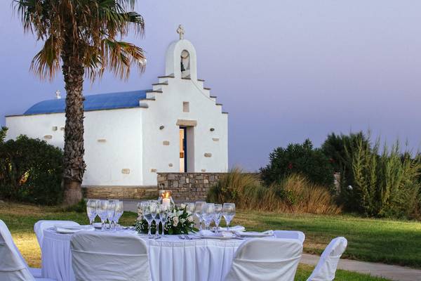 Außenbereich des Poseidon of Paros Hotel & Spa mit gedecktem Tisch und Kirche im Hintergrund