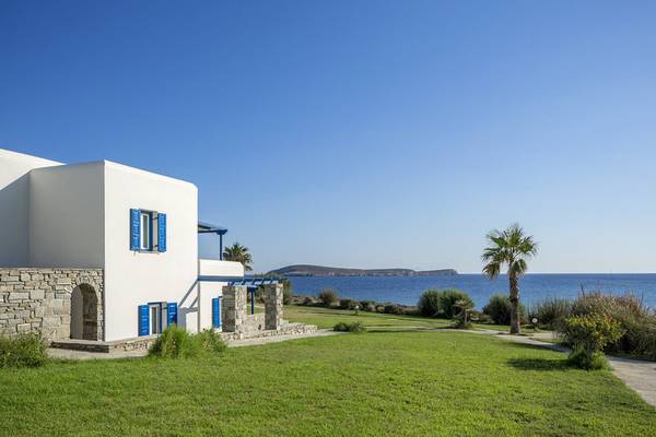Poseidon of Paros Hotel & Spa Außenansicht mit weißem Gebäude, blauen Fensterläden und Blick auf das Meer.