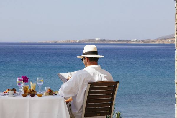 Ein Mann liest Zeitung und genießt das Frühstück auf einer Terrasse mit Blick auf das Meer, im Poseidon of Paros Hotel & Spa.