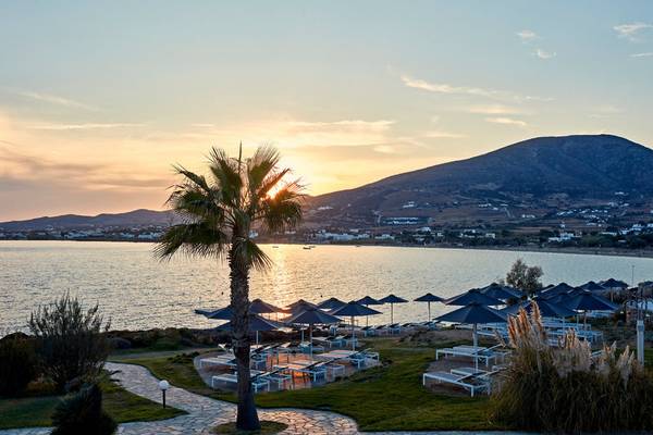 Sonnenuntergang am Strand des Poseidon of Paros Hotel & Spa mit Palme und Sonnenschirmen.