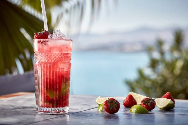 Roter Cocktail mit Erdbeere und Limettenscheiben auf einem Tisch mit Blick auf das Meer