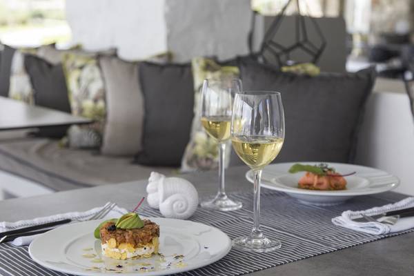 Ein Tisch mit Speisen und Getränken, einschließlich zweier Gläser mit Weißwein, einem Teller mit Vorspeise und einem weiteren Teller mit Hauptgericht.