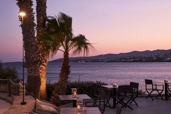 Abendliche Aussicht auf den Außenbereich des Poseidon of Paros Hotel & Spa mit Tischen und Stühlen am Meer.