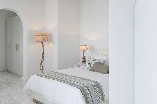 Schlafzimmer im Poseidon of Paros Hotel mit weißen Wänden, einem Bett und zwei Lampen.