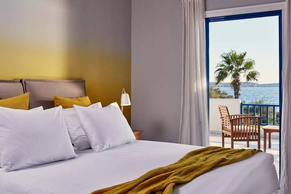 Schlafzimmer im Poseidon of Paros Hotel mit Bett, Kissen und Balkon mit Blick aufs Meer.